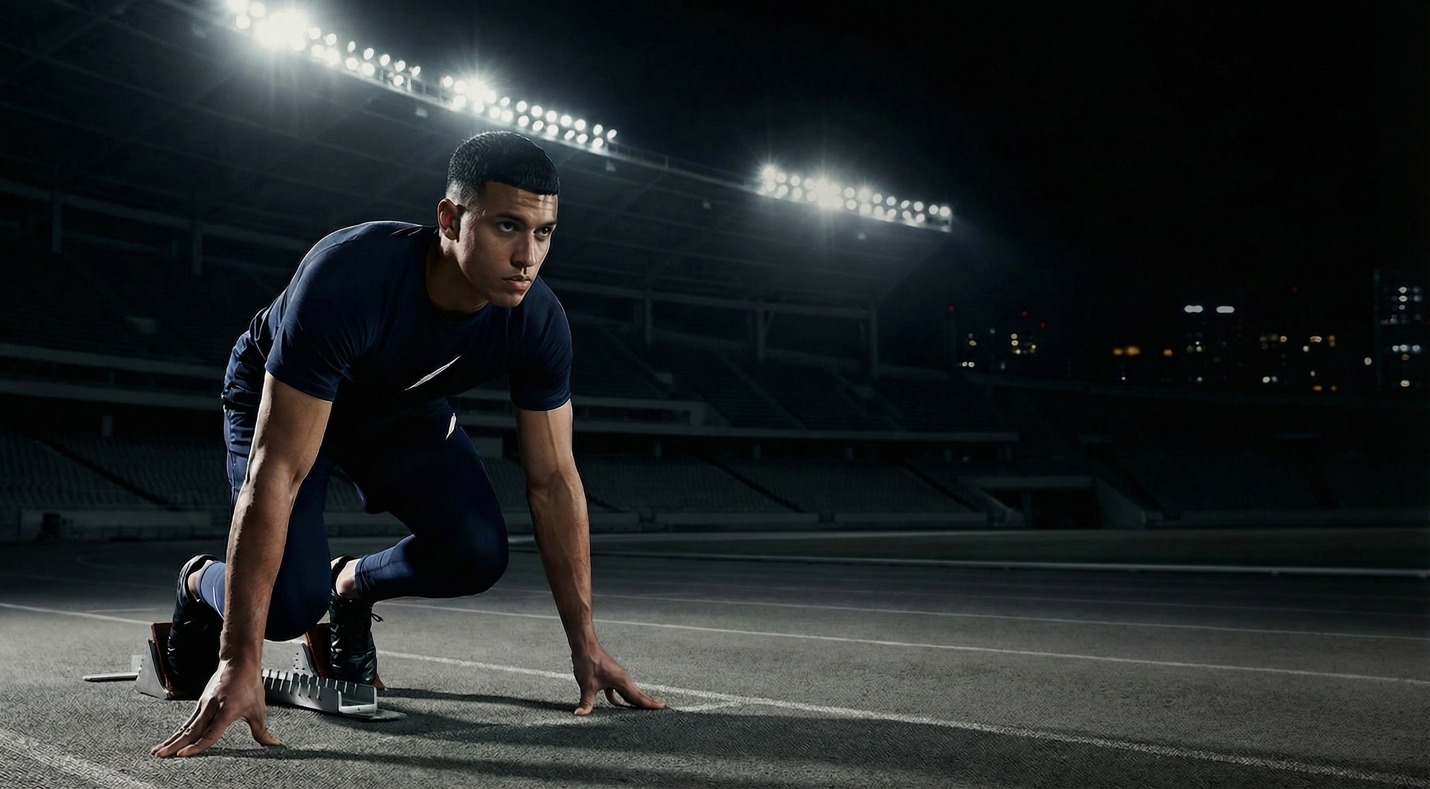 Athlet im Startblock trägt dunkelblaues Performance-Set im Stadion bei Nacht